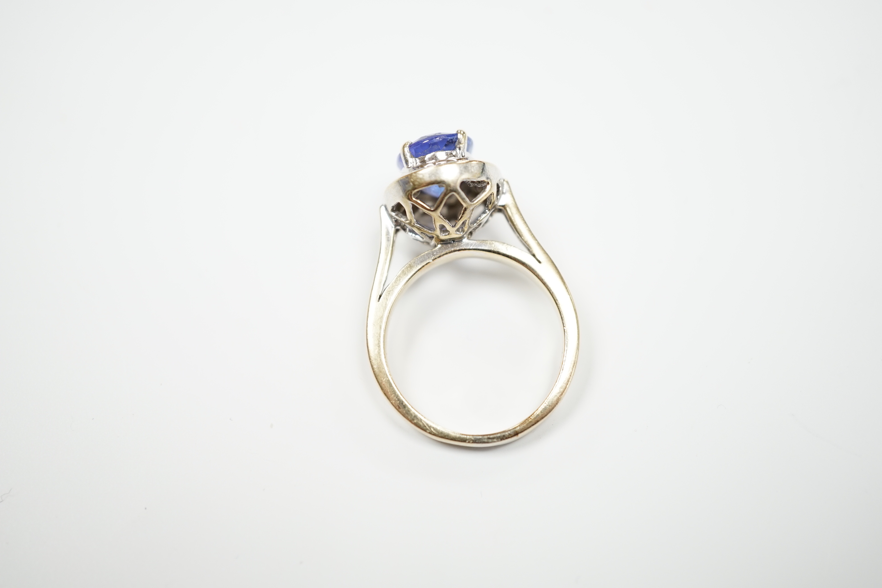 A modern 750 and oval cut single stone tanzanite(worn) set dress ring, with diamond set border and shoulders, size P, gross weight 8.9 grams.